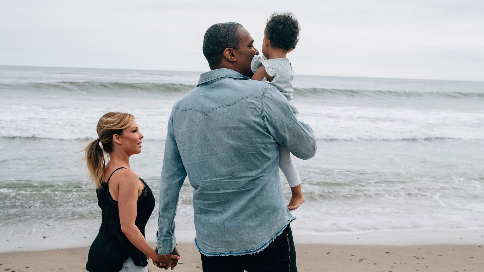 A family of three walking along the beach.